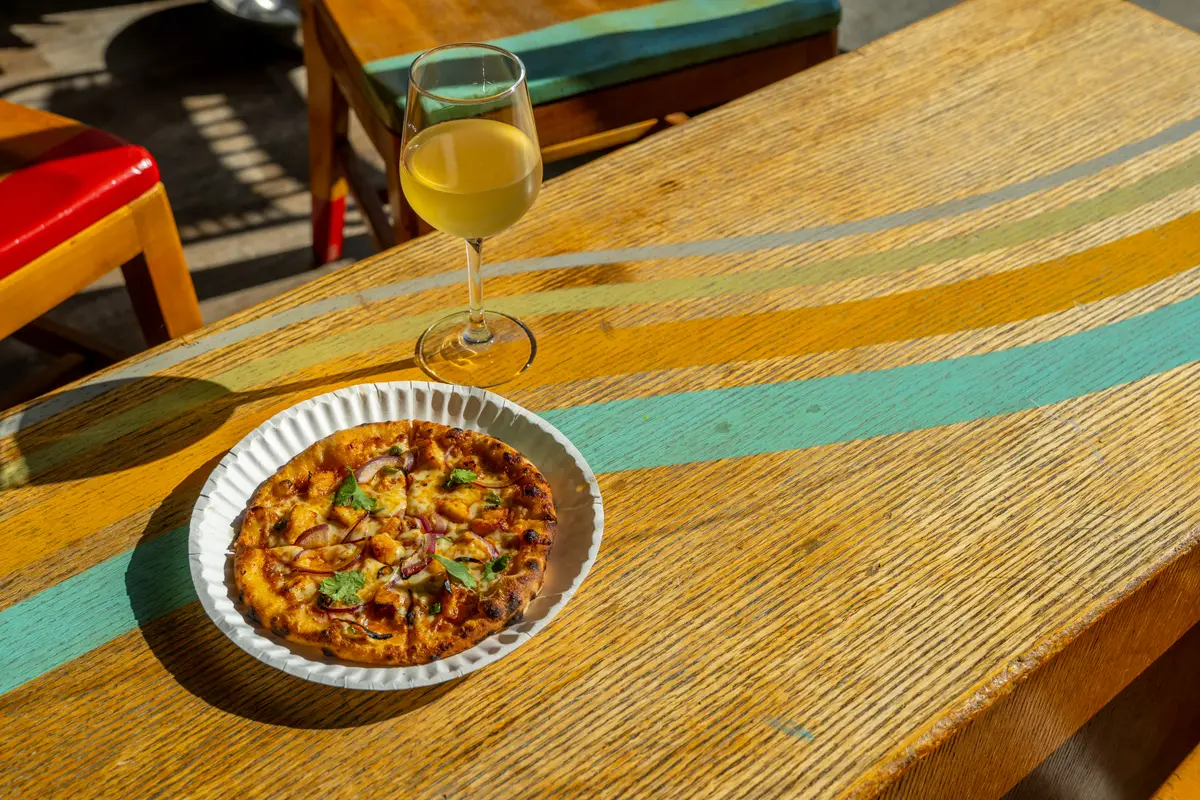 A glass of natural white wine next to a pizza on a table at Ballard Beer Box in Ballard, Seattle