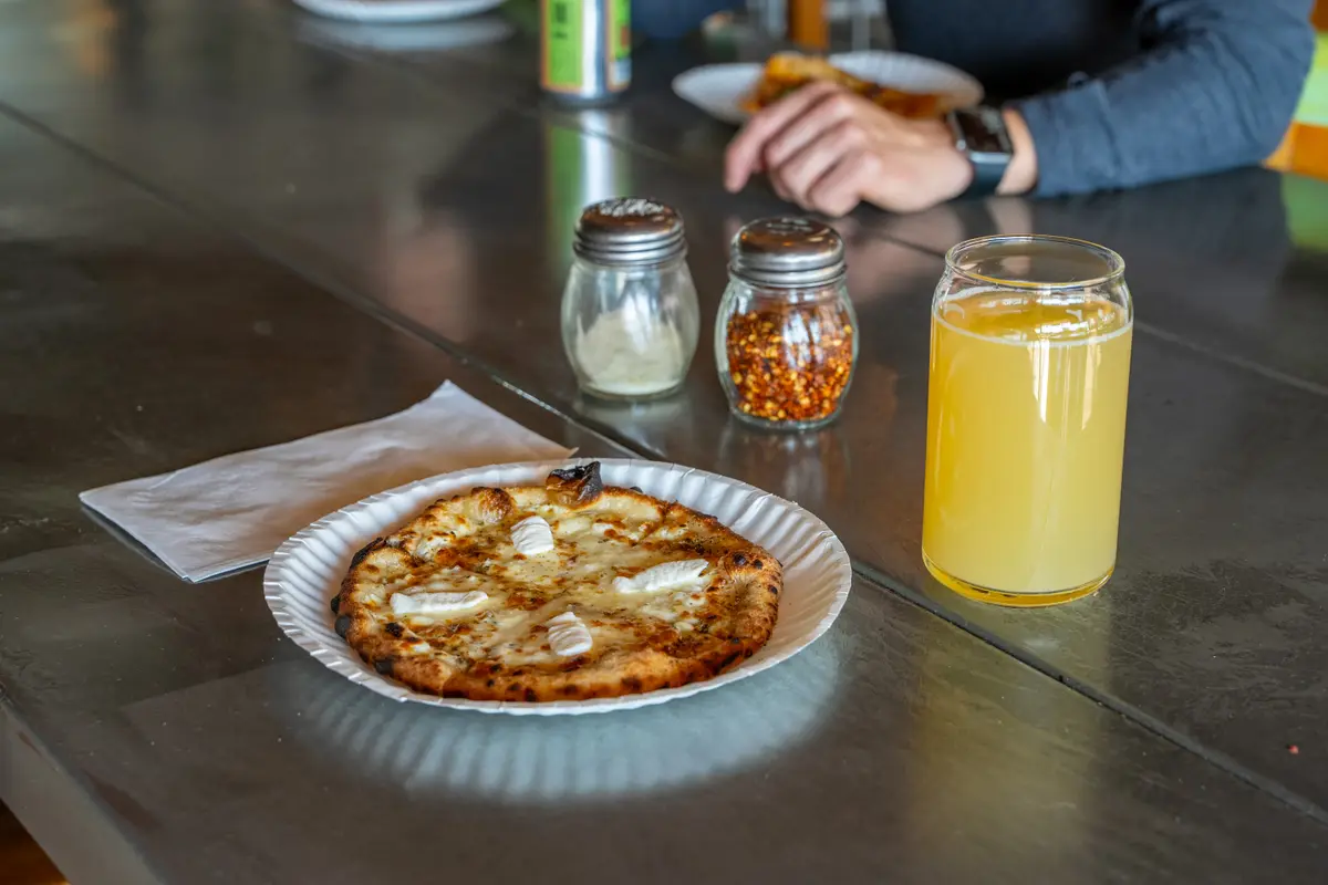 A pale craft beer beside a pizza on a table at Ballard Beer Box in Ballard, Seattle